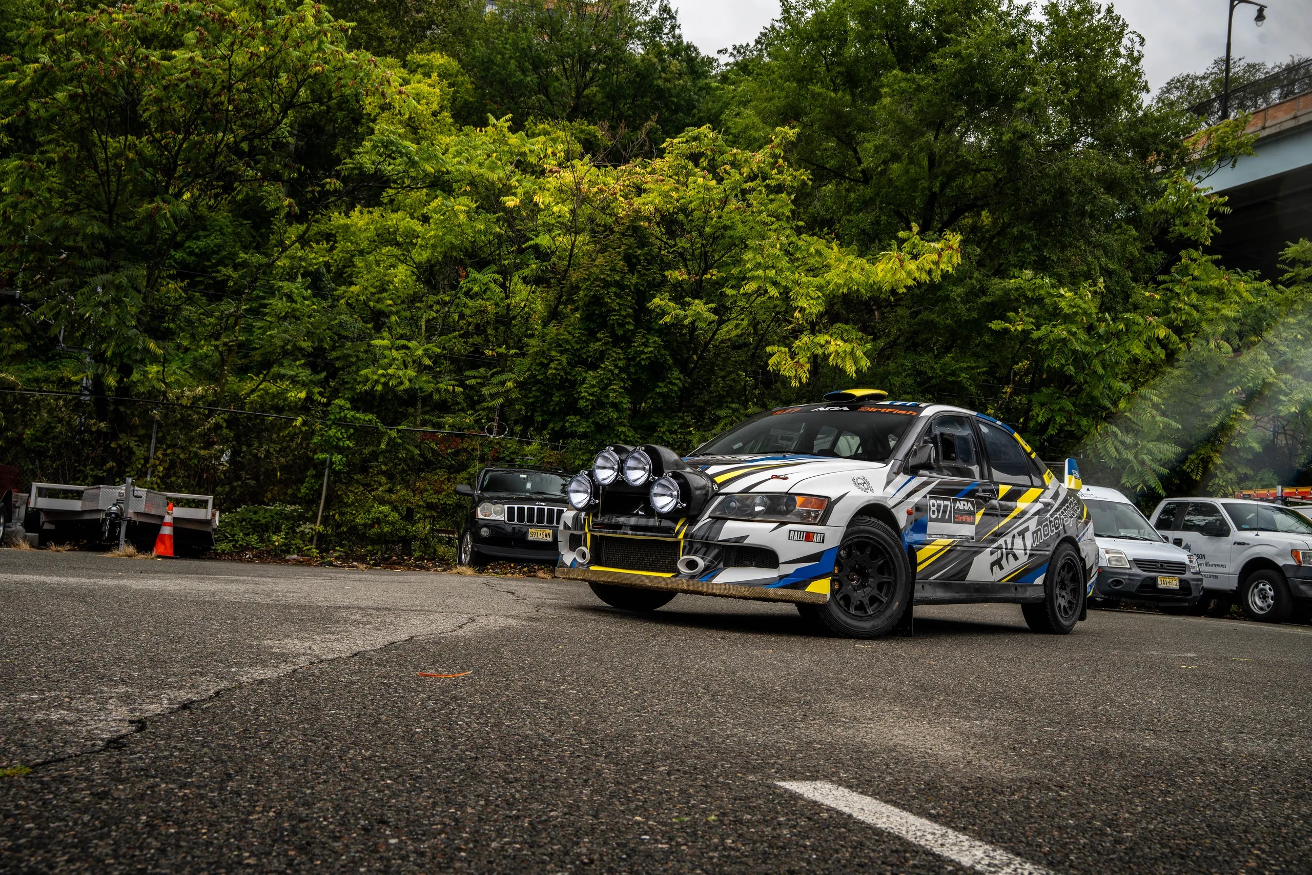 RKT Mitsubishi Evo 8 rally car on a wet road surrounded by green trees