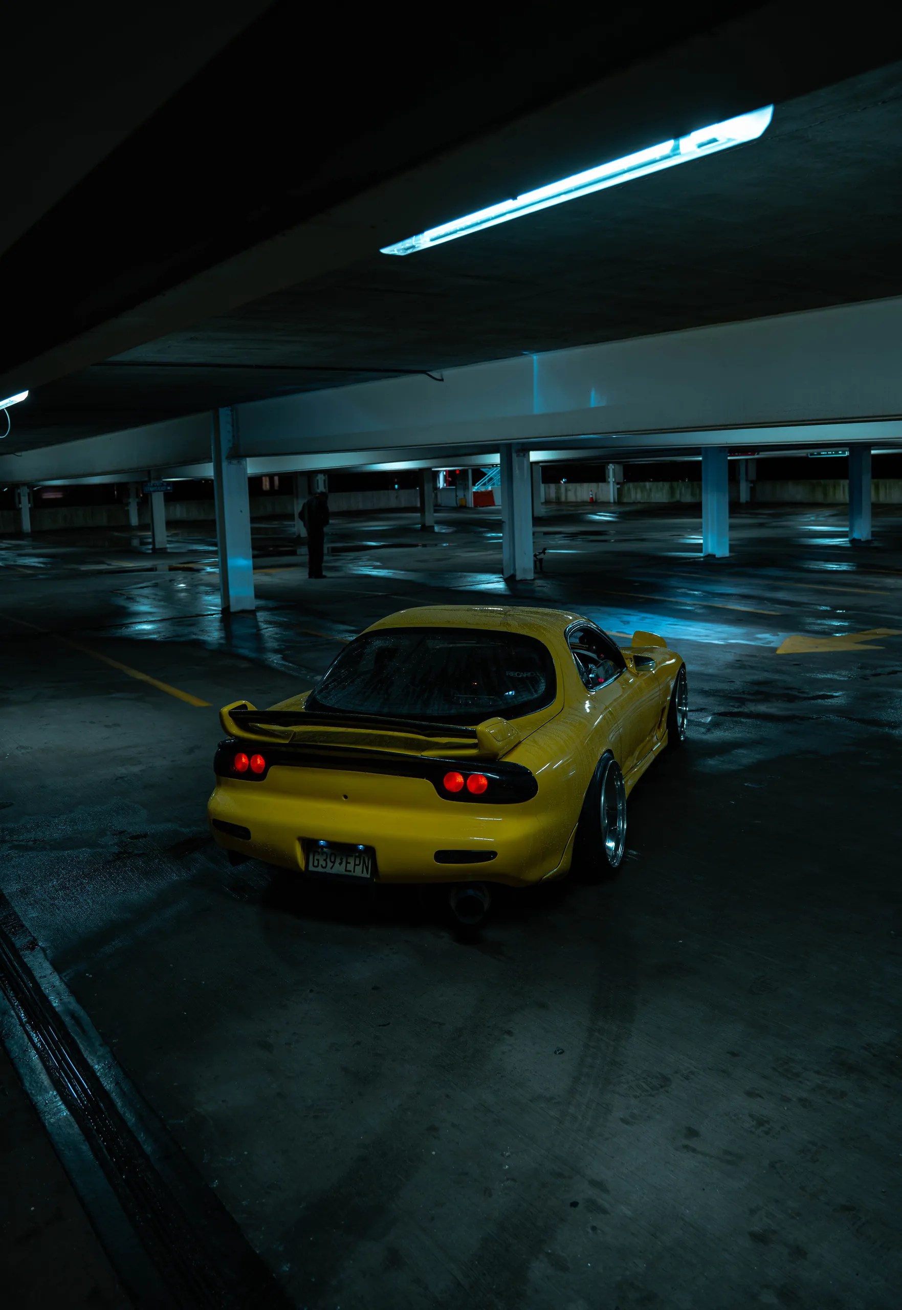 Vertical shot of a yellow Mazda RX7 FD from behind in an empty Jersey City parking garage
