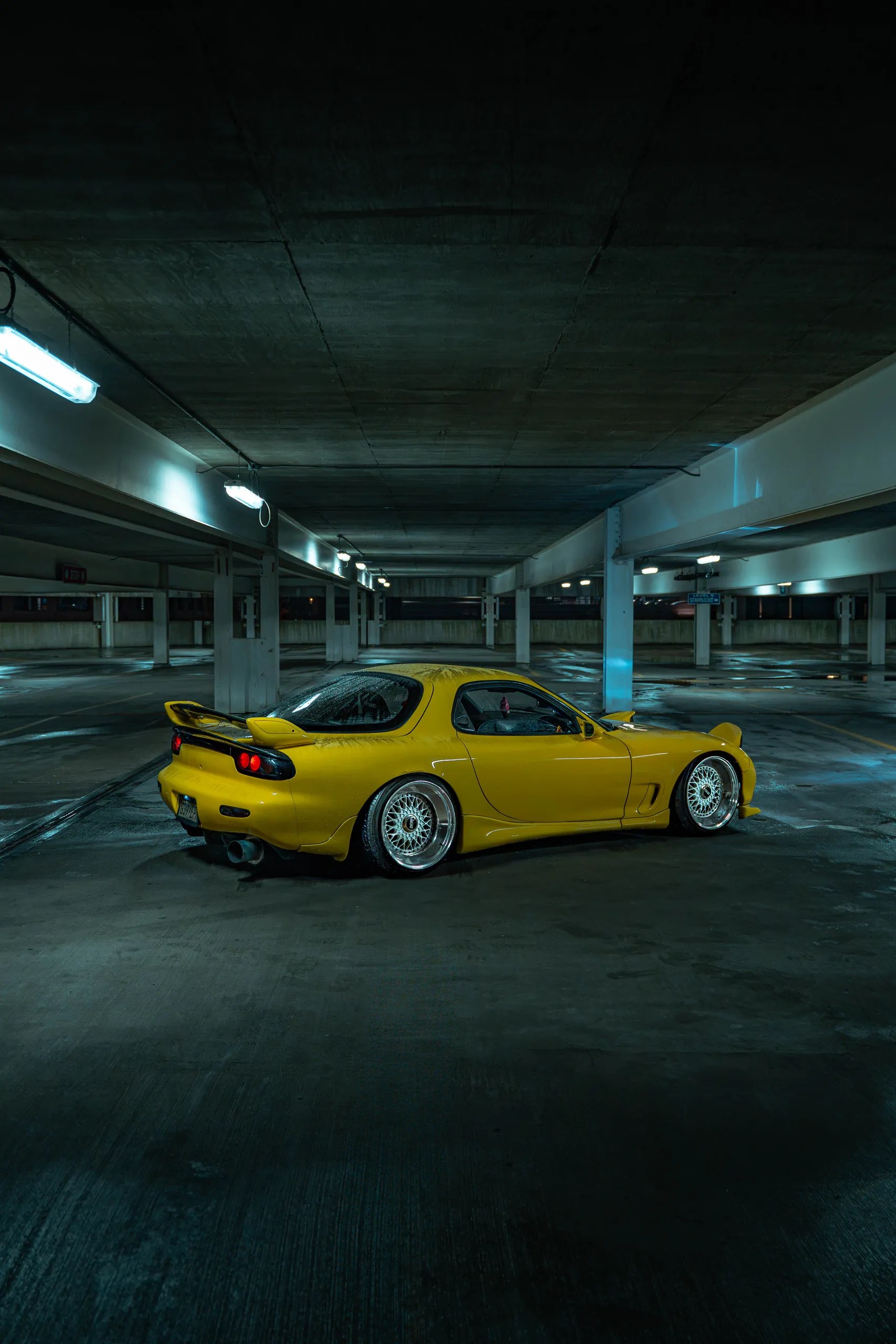 Vertical side profile of a yellow Mazda RX7 FD under fluorescent lights in a parking garage