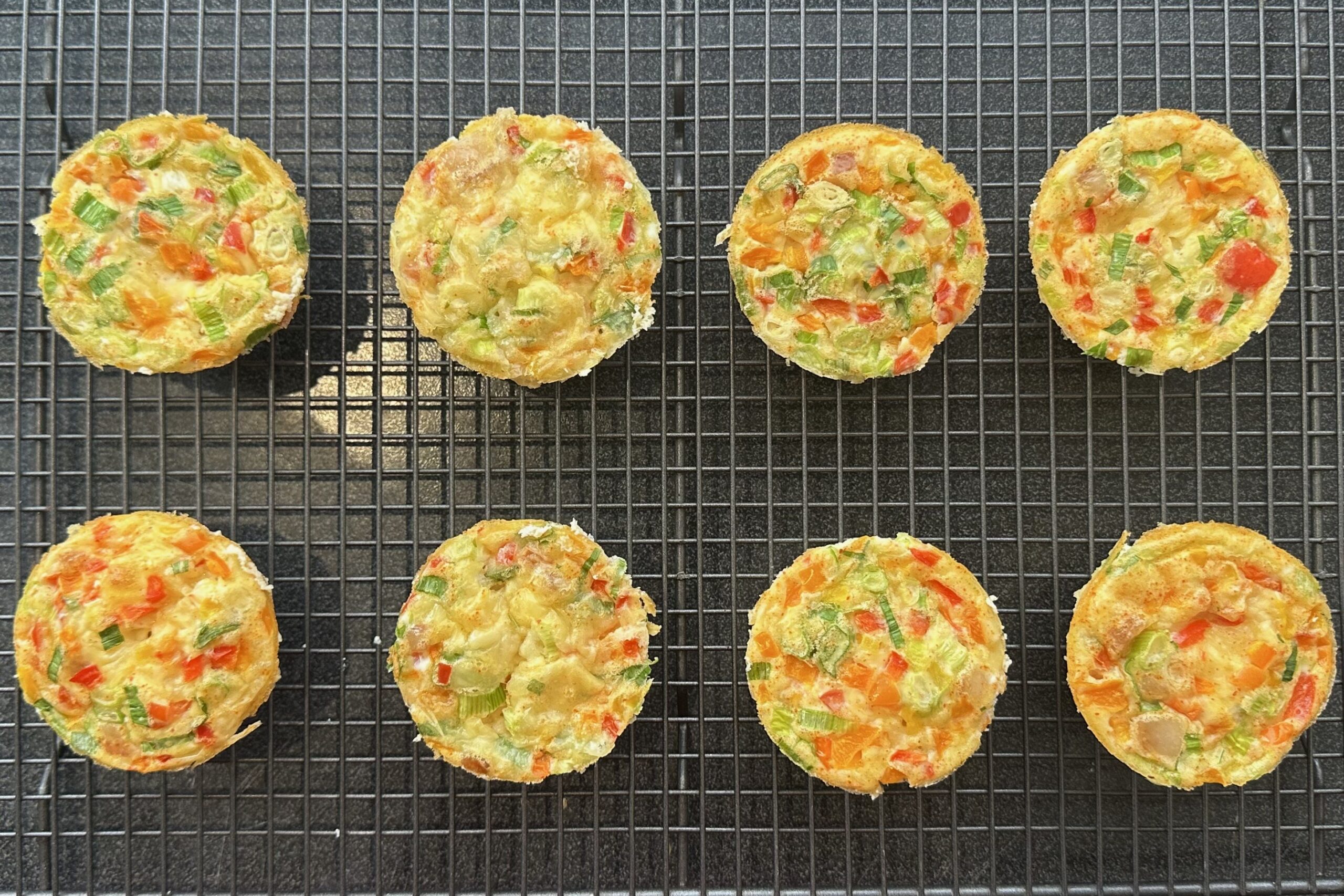 Breakfast egg muffins with different fillings on a baking rack.