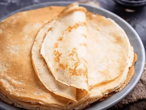 Crêpes maison fines empilées sur une assiette, bords dentelés et dessous tacheté de brun