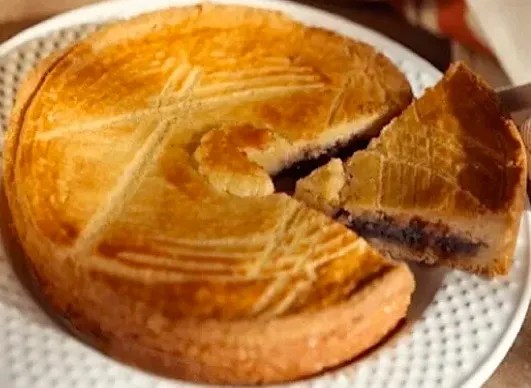 Gâteau basque aux cerises doré et rayé à la fourchette, une part coupée montrant la couche de confiture de cerises noires