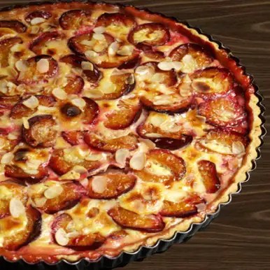Tarte alsacienne aux quetsches en rosace sur pâte sablée, appareil à la crème pris et amandes effilées dorées