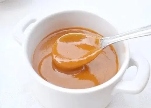 Caramel au beurre salé maison nappant une crêpe, pot de sauce au caramel en arrière-plan