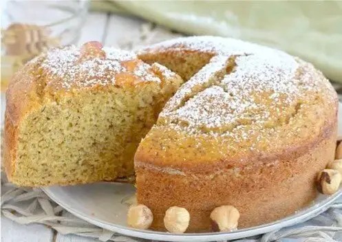Gâteau au miel et aux noisettes moelleux saupoudré de sucre glace, pot de miel et noisettes à côté