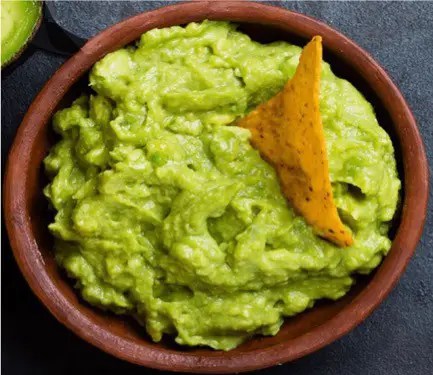 Guacamole maison dans un bol, avocat écrasé avec tomate, oignon rouge et coriandre