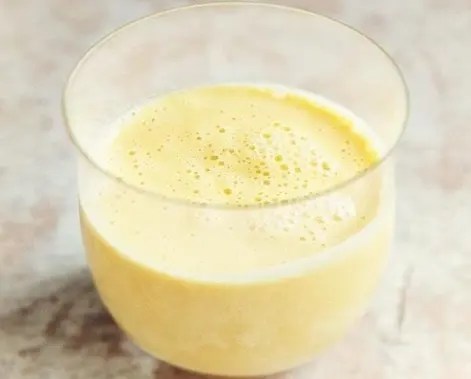 Lassi à la mangue servi dans un verre, parsemé de pistaches concassées