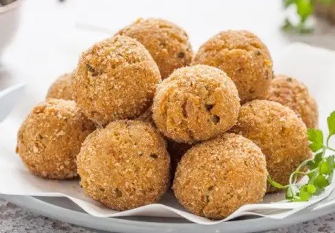 Boulettes de thon au mascarpone panées et frites, dorées, dans un plat de service avec un quartier de citron