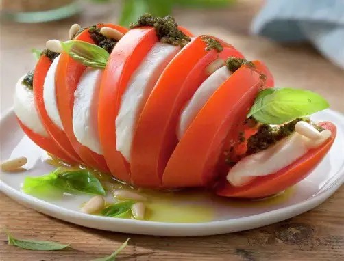 Tomates accordéon garnies de mozzarella et de basilic, nappées de pesto et parsemées de pignons grillés