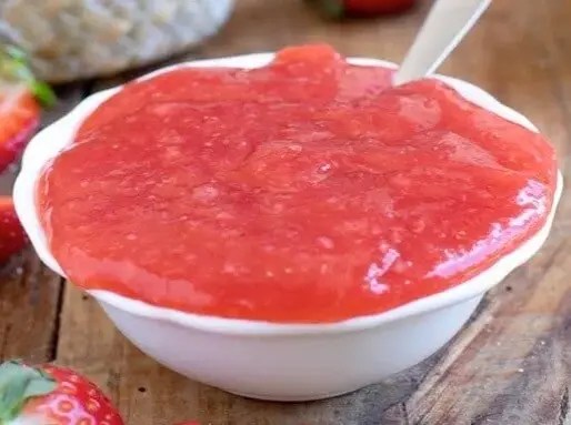 Crème de fraises rouge dans un bocal, tartinée sur une tranche de brioche