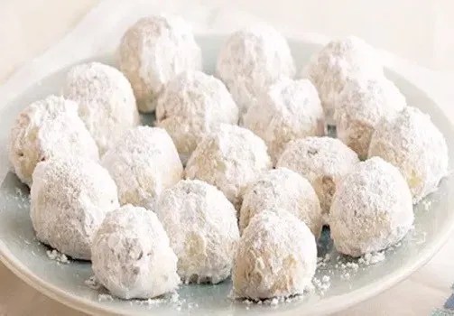 Polvorones aux noix roulés dans le sucre glace, disposés sur une assiette de Noël