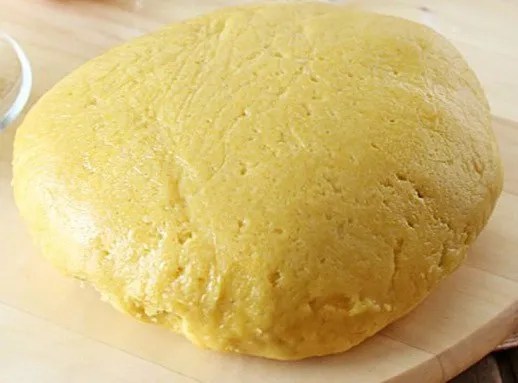 Pâte brisée à la crème en boule sur un plan de travail fariné, à côté d'un rouleau à pâtisserie