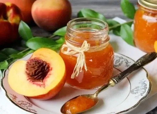 Confiture de pêches grand-mère en pot, morceaux de pêches fondants et feuilles de pêcher