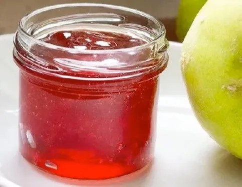 Gelée de coings maison couleur ambre dans un pot, à côté de coings jaunes