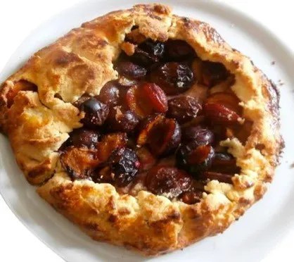 Tarte rustique aux quetsches sur sa plaque, bords de pâte repliés en plis irréguliers et dorés sur les demi-prunes