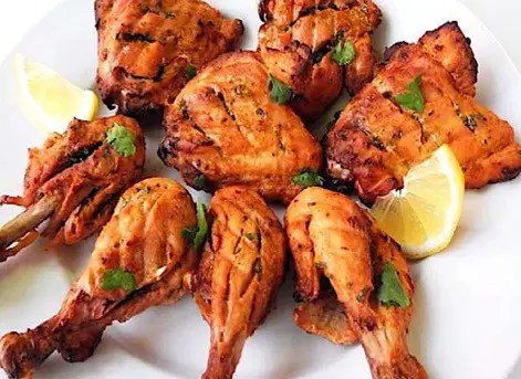 Poulet tandoori grillé, rouge-orangé, servi avec citron et oignons