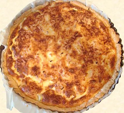 Quiche alsacienne dorée, oignons fondants et lardons sous une migaine aux œufs, une part découpée