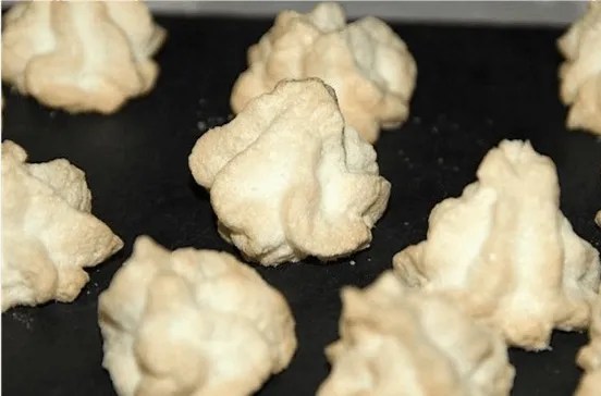 Meringues très légères blanches dressées à la poche à douille sur une plaque, sans coloration