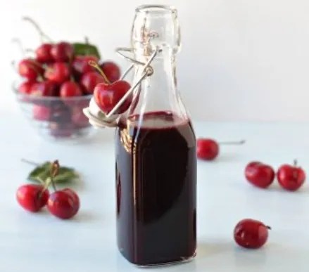 Sirop de cerise maison rouge foncé dans une bouteille, avec des cerises fraîches