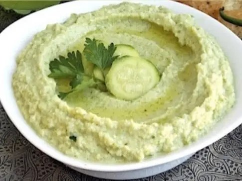 Houmous de courgettes crues dans un bol, filet d'huile d'olive et graines de cumin