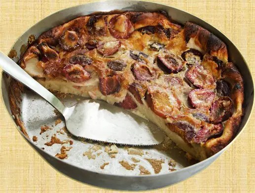 Flan alsacien aux quetsches doré dans son moule, demi-prunes bleues sur le dessus saupoudrées de sucre glace