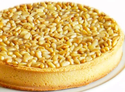 Tarte aux pignons provençale dorée, part découpée montrant la crème d'amandes sous les pignons grillés