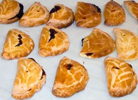 Rissoles aux pruneaux en demi-lune, dorées, l'une coupée montrant la crème de pruneaux