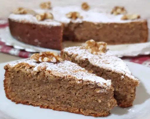 Gâteau aux noix à 3 ingrédients saupoudré de sucre glace, décoré de noix