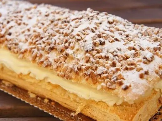 Gâteau feuilleté à la crème pâtissière, doré et parsemé d'amandes, coupé en parts