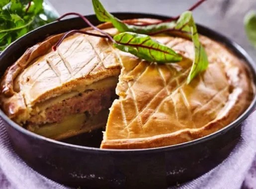 Pâté de pommes de terre corrézien doré, une part coupée sur ses couches de pommes de terre, saucisson à l'ail et crème prise