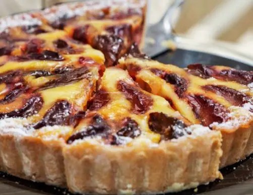 Tarte aux prunes à l'alsacienne dorée, tranches de prunes en rosace sous un flan crémeux, une part découpée