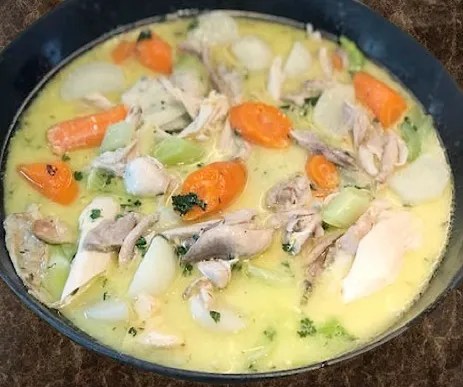 Waterzoï de volaille servi en assiette creuse, morceaux de poulet et julienne de légumes dans un bouillon crémé au persil
