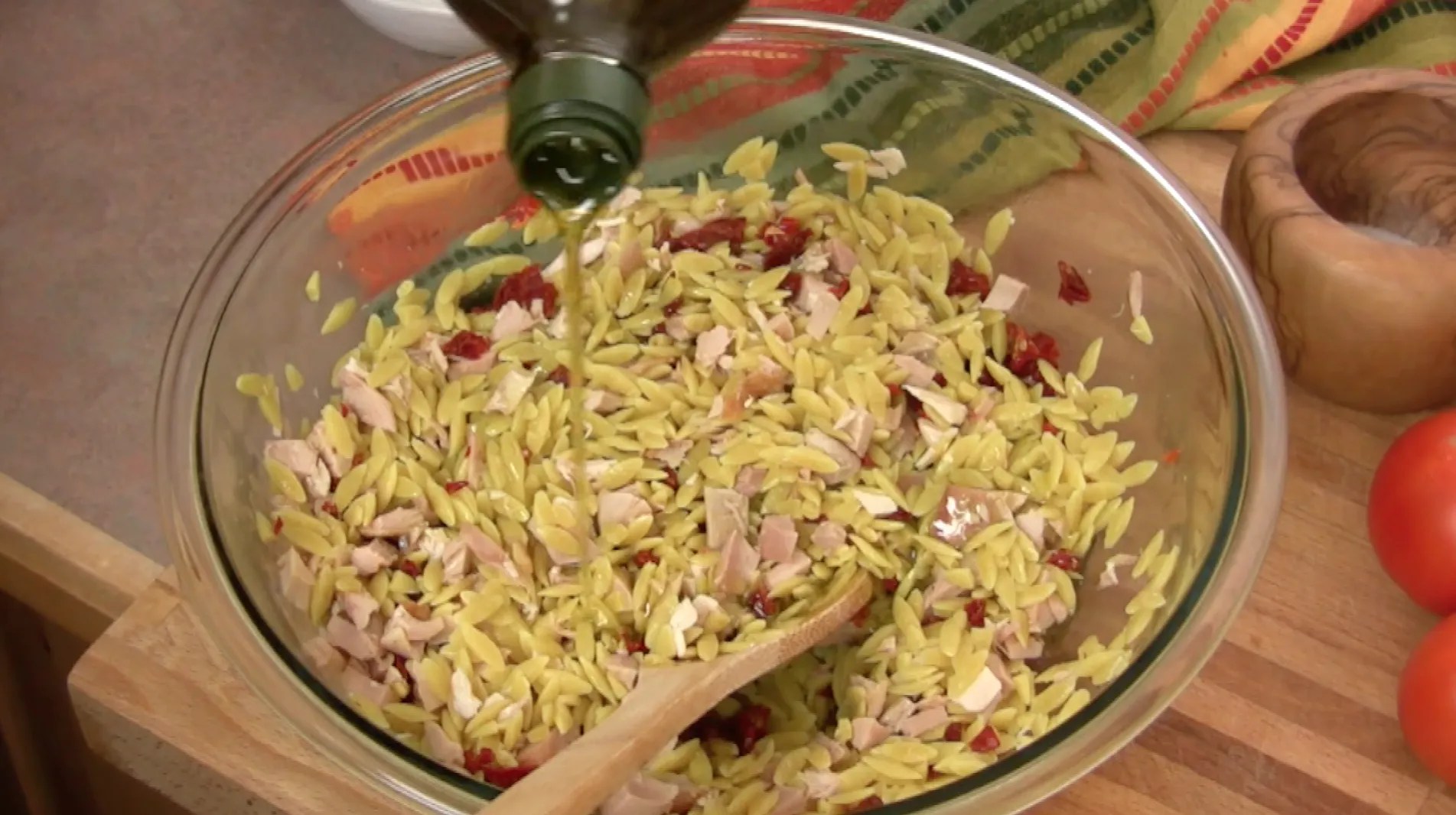 Adding olive oil to orzo, chicken and sun dried tomatoes