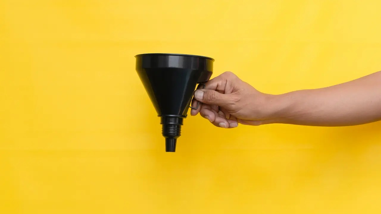 Hand holding a black funnel against a bright yellow background.