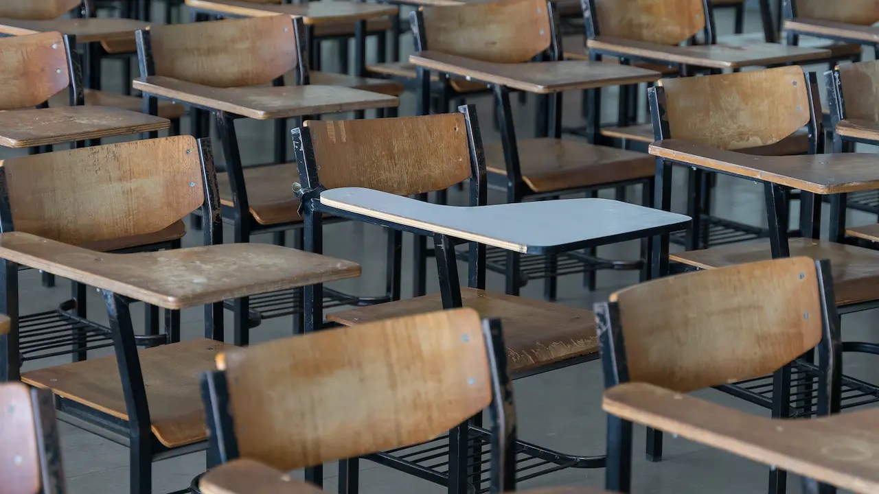Empty wooden student desks in rows in a vacant classroom.