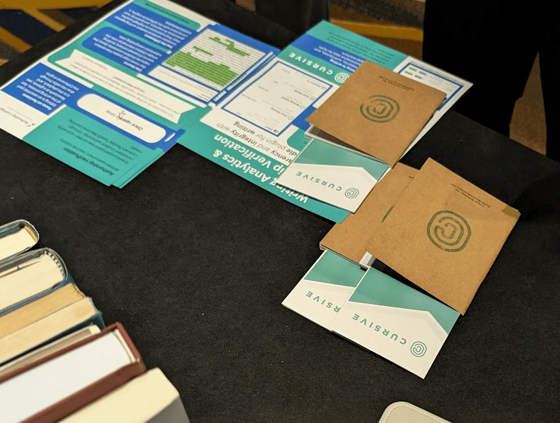 A display table featuring informational materials and brochures from Cursive, including a report and feedback forms.