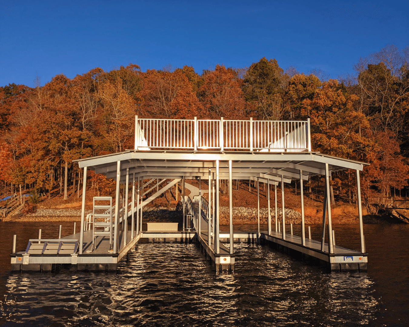 Custom dock with a rooftop deck, set against a backdrop of vibrant fall foliage and clear blue skies over a lake.