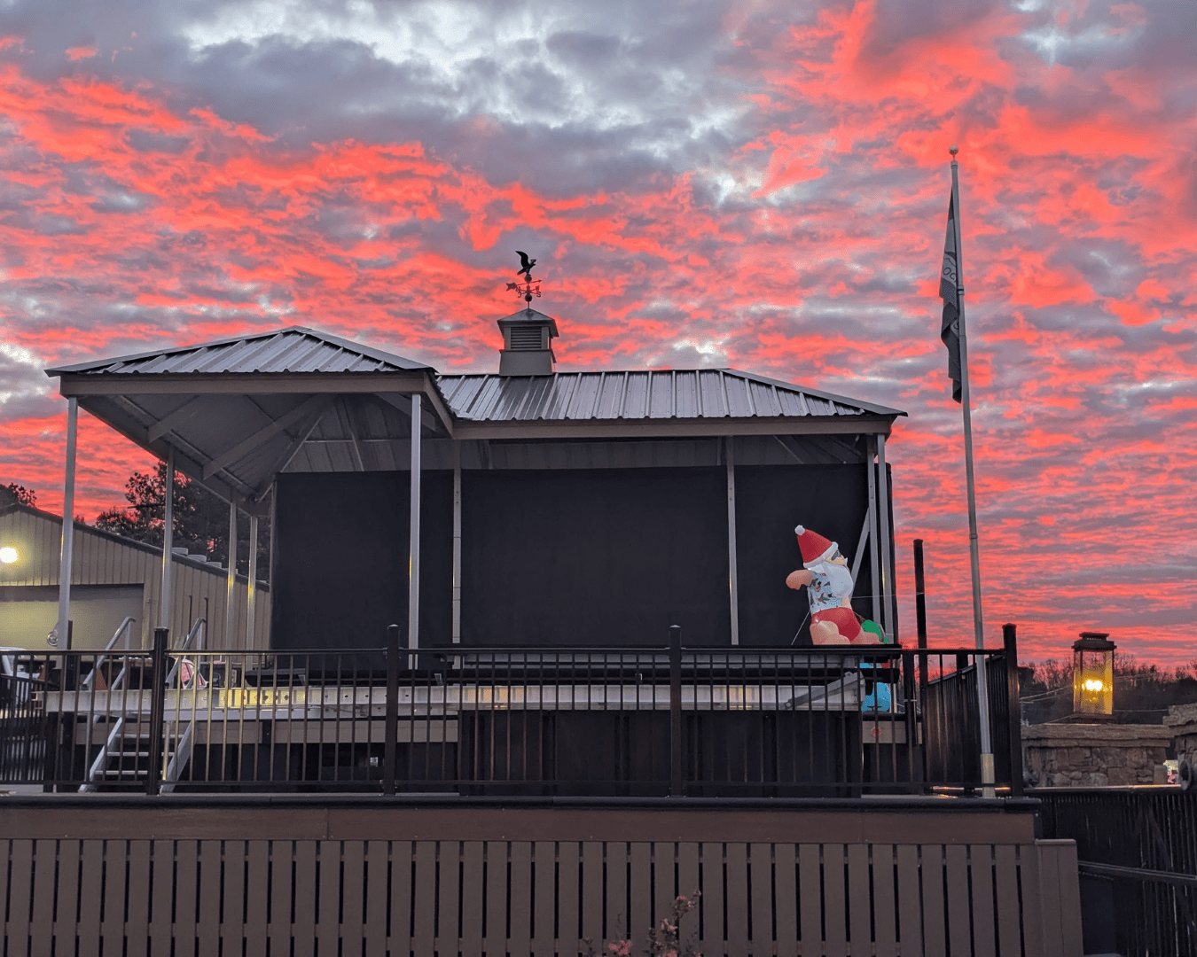 Covered dock structure at sunset with vibrant pink and orange clouds, a flagpole, and a festive inflatable Santa decoration on the deck.