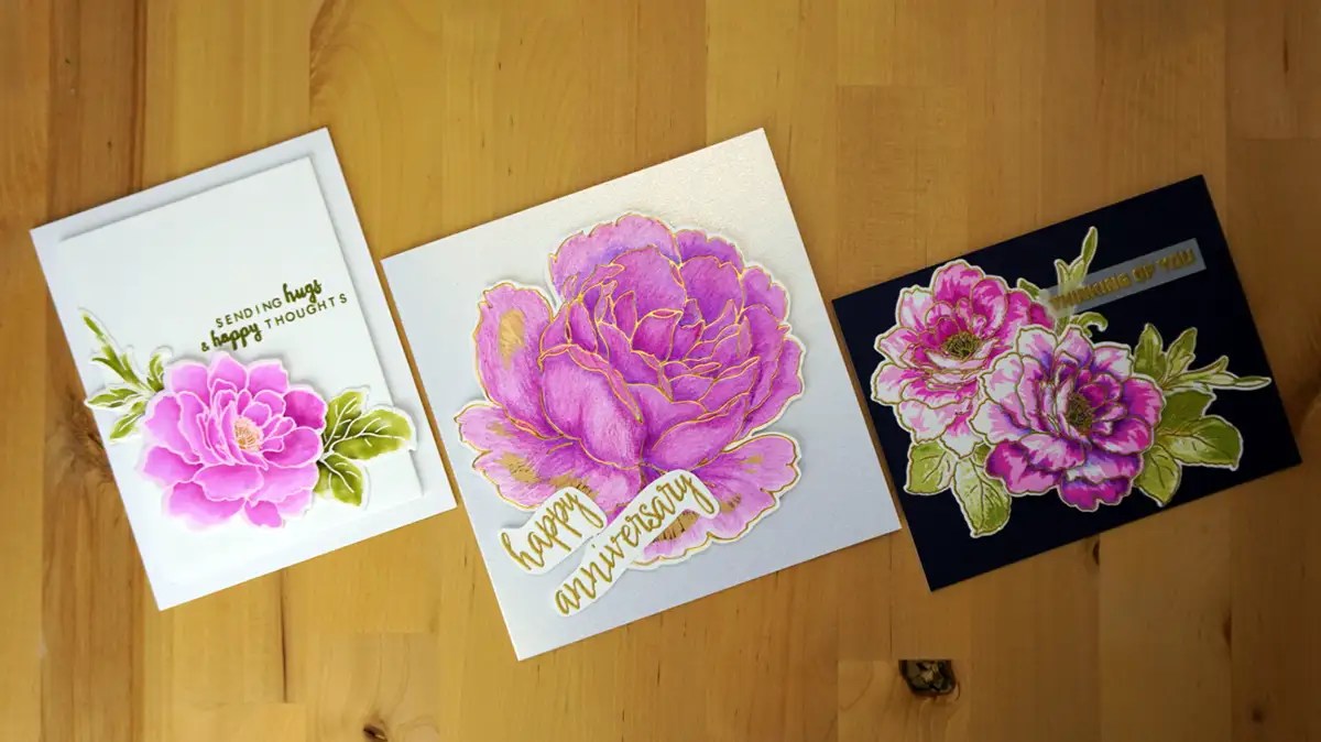 Three magenta greeting cards with floral designs and various messages are placed on a wooden surface. The card on the left reads "Sending hugs & happy thoughts," the middle card says "happy anniversary," and the card on the right reads "thankful for you." Enter our giveaway to win these beautiful cards!