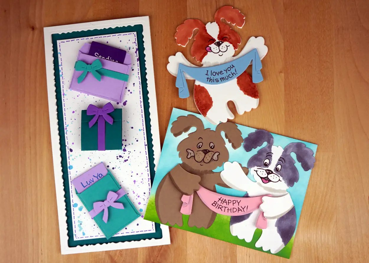 Three cute cards are displayed: one featuring gift boxes with ribbons, and two others with dog illustrations holding birthday and love messages. The DIY cards are laid out on a wooden surface.