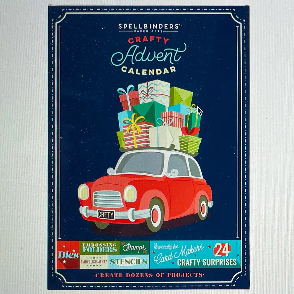A red car carrying a stack of colorful wrapped gifts is illustrated on the cover of the 2023 Crafty Advent Calendar from Spellbinders, which advertises 24 crafty surprises including dies, stamps, and stencils.