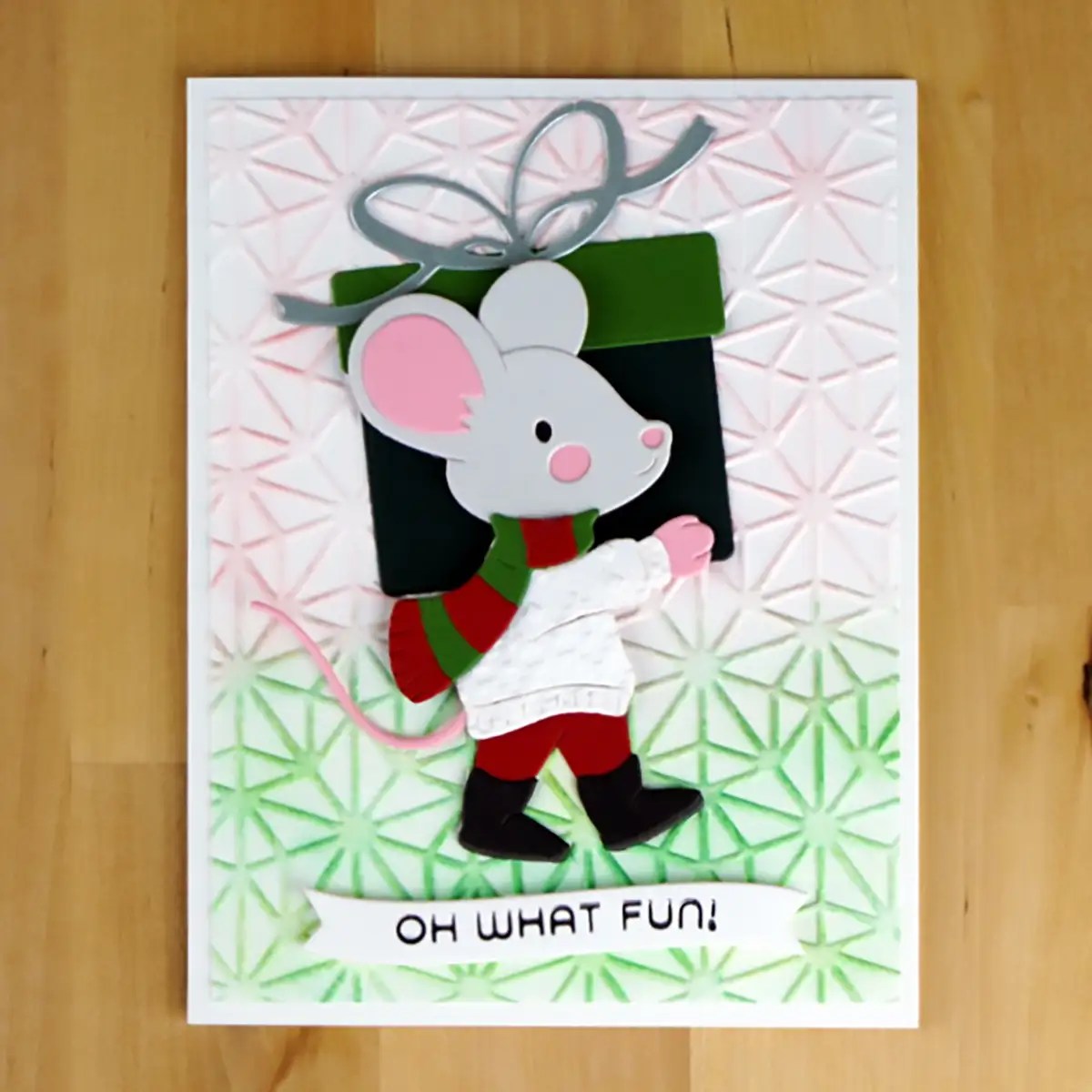 Handmade holiday card featuring a festive Dancin' & Giftin' Mouse in a scarf and boots, carrying a gift box. The background has a textured geometric pattern, with a text ribbon at the bottom reading "OH WHAT FUN!".