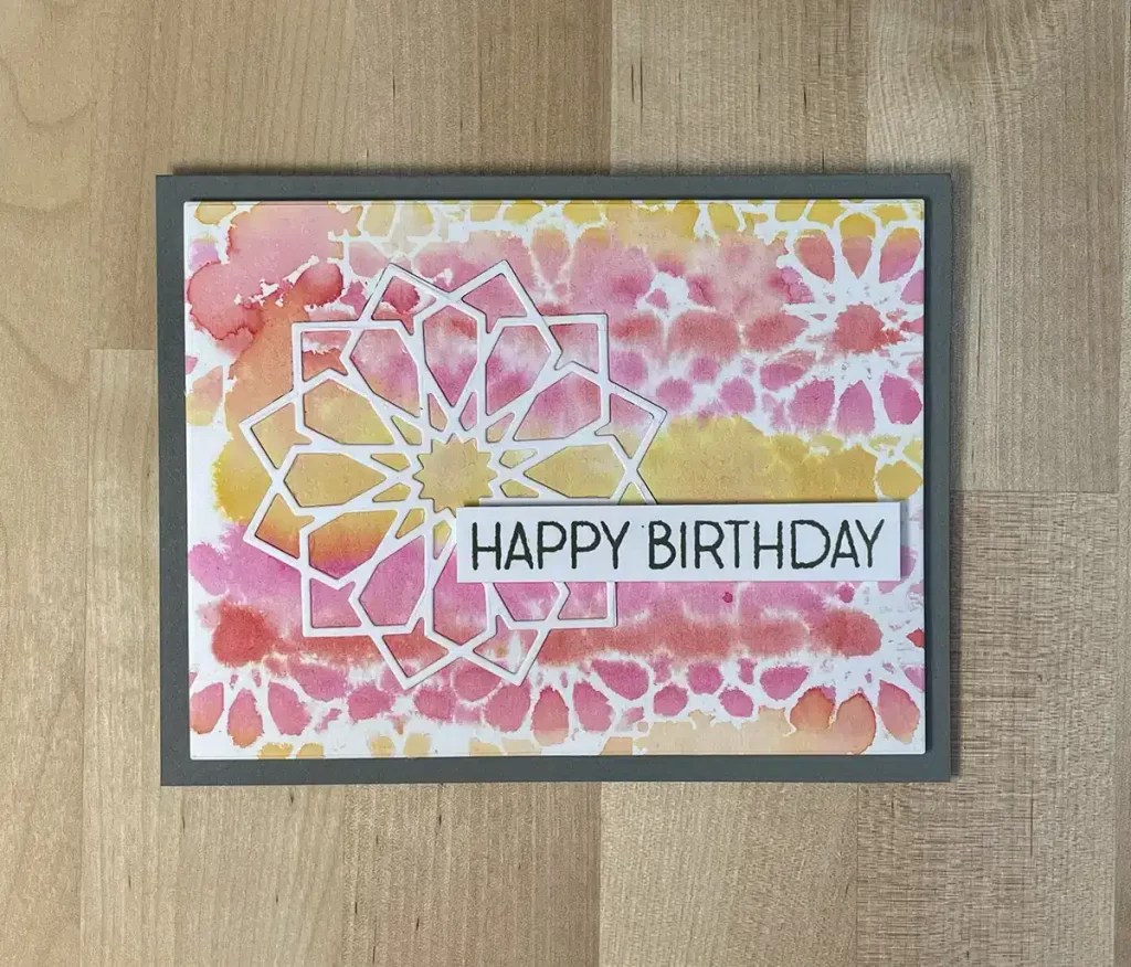 A jaw-dropping birthday card with a colorful, abstract design and the text "HAPPY BIRTHDAY" on the front. The background features pink, yellow, and white hues with geometric patterns. This card is part of an exclusive card set perfect for any celebration.