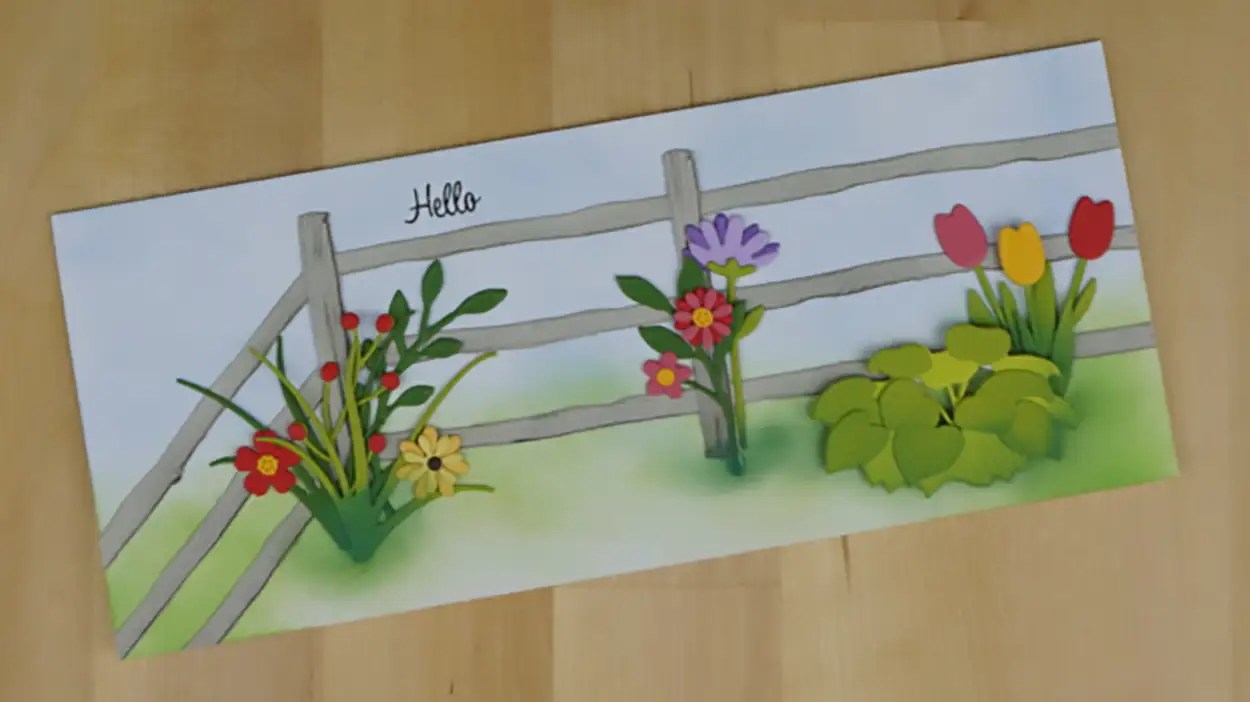A greeting card with a "Hello" message featuring a garden with various colorful flowers and a wooden fence on a light wooden surface, evoking the serene charm of country roads.
