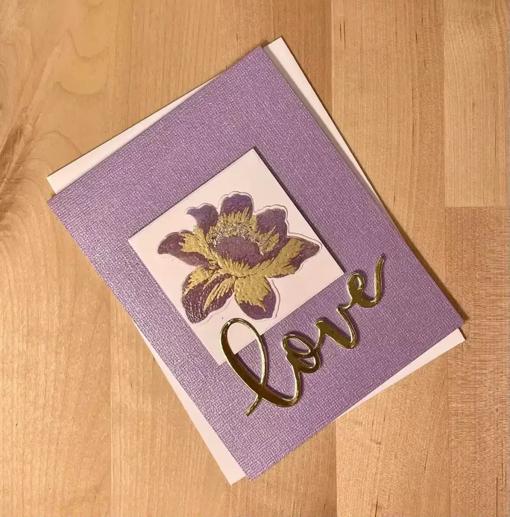 A purple and gold card with the word love on it, created using heat embossing techniques.