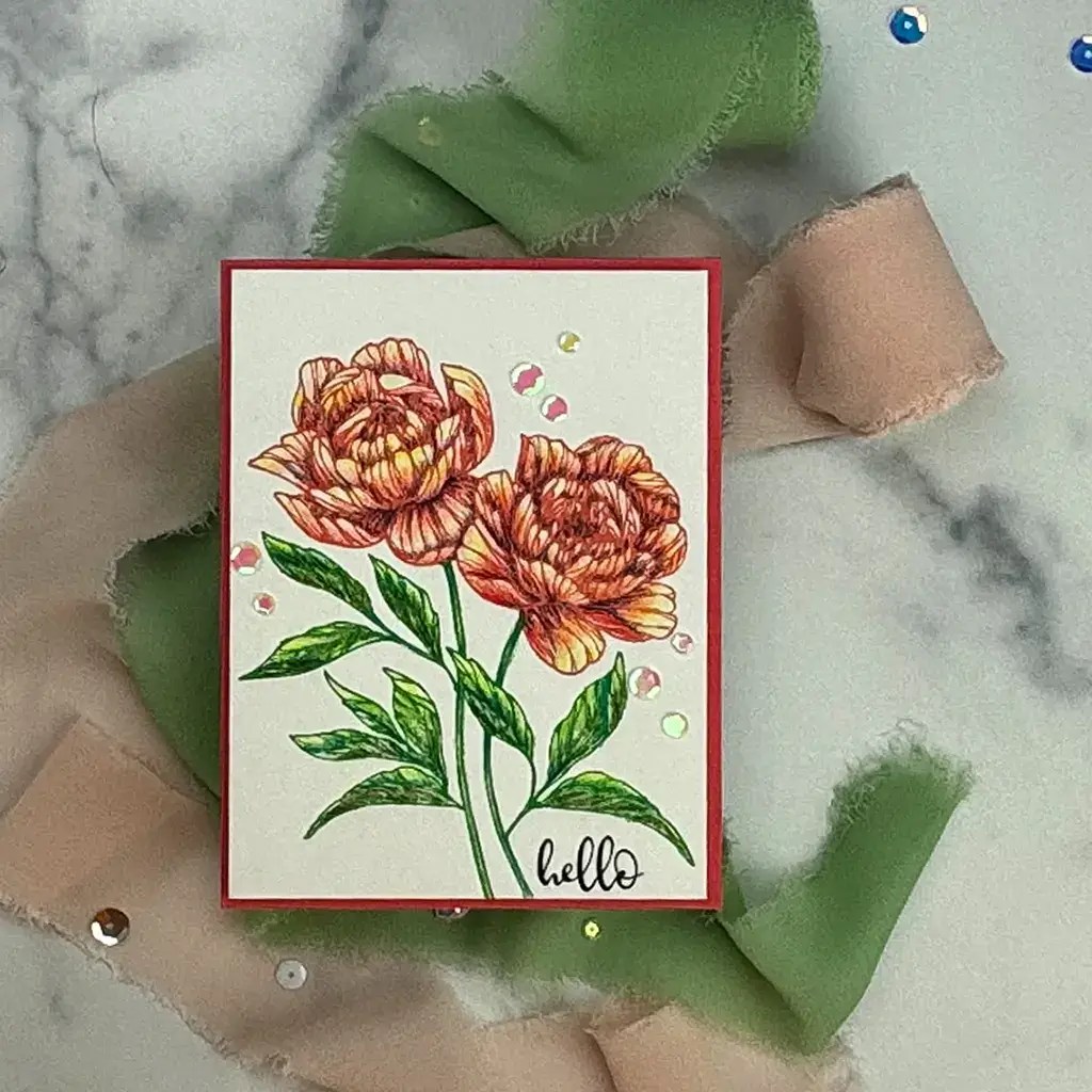 A greeting card with floral artwork features two orange peonies on a red-bordered white background with the word "hello." The card, embodying peony perfection, is decorated with green and beige fabric strips and scattered rhinestones.