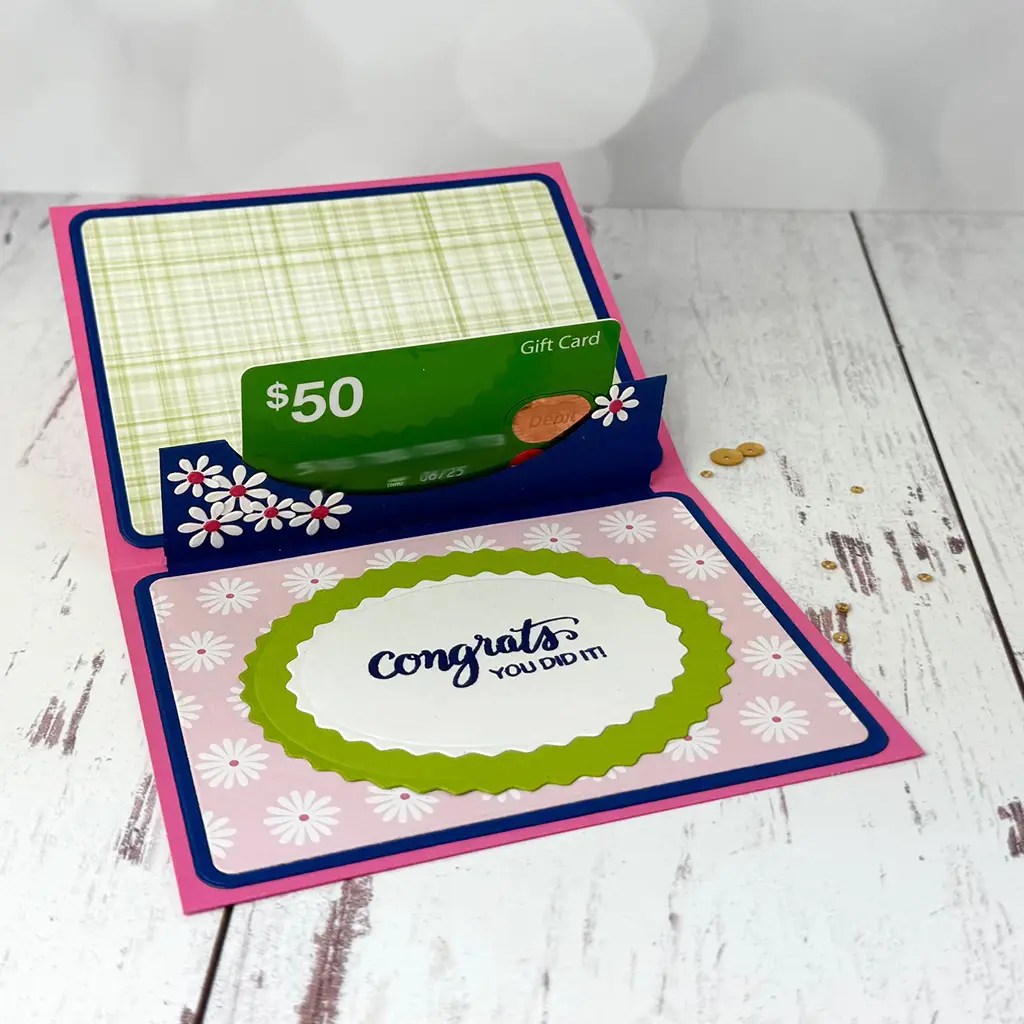 Open greeting card with "Congrats you did it!" message and a $50 gift card tucked inside. The card, crafted with beautiful floral patterns—a true masterpiece of cardmaking—is placed on a light wooden surface, ready to convey heartfelt sentiments.