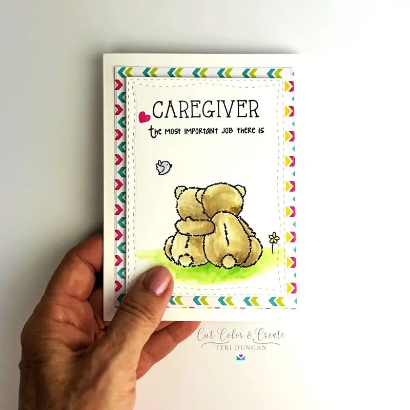 Hand holding a greeting card featuring a cute, illustrated bear hugging a small bear with the text: "Caregiver, the most important job there is" and a colorful border.