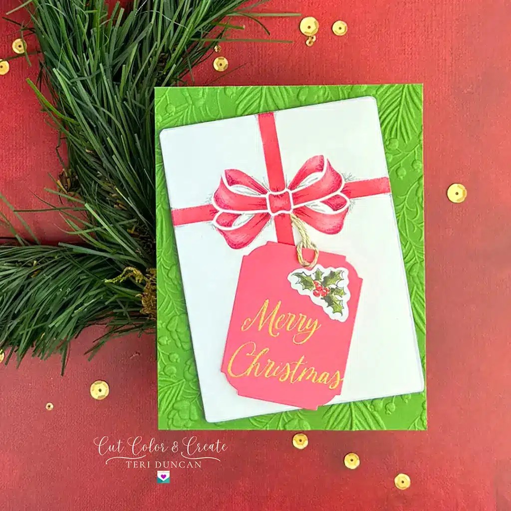 A Christmas card from Spellbinders Monthly Clubs features a white envelope with a red ribbon and a tag reading "Merry Christmas." Set against a green leafy background with fir branches and gold sequins as decoration, it's the perfect preview for the upcoming July 2024 collection.