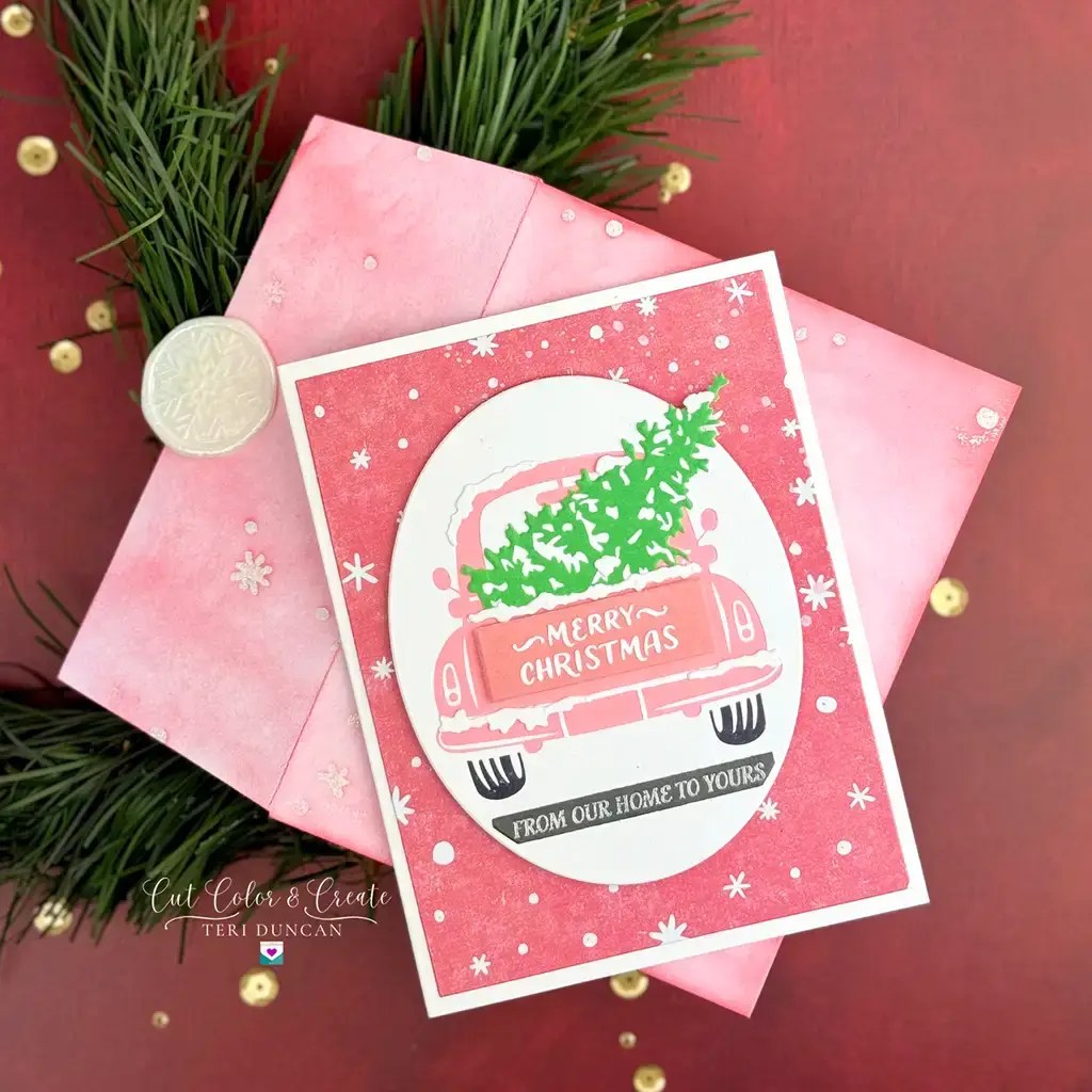 Christmas card featuring a pink car with a tree on its roof, with the words "Merry Christmas" and "From Our Home to Yours," placed on a red patterned background beside a pink envelope and fir branches. This exclusive design is part of the Spellbinders July 2024 collection.